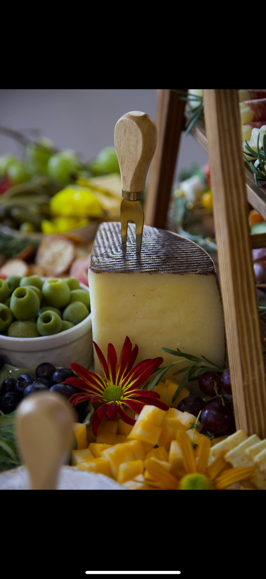 Elevated grazing display with artisan cheese, olives, fruit, and edible florals